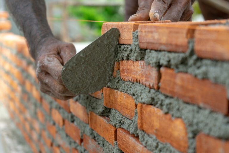 Closeup red bricklayers wall and trowel with dirty hands of work